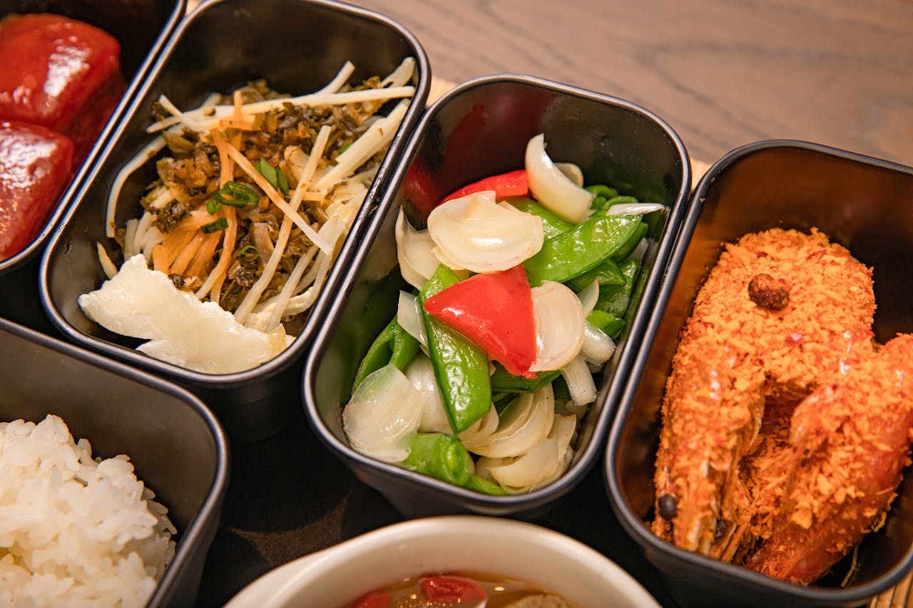 Colorful bento box featuring crispy shrimp, sautéed vegetables, and rice, perfect for a healthy meal.