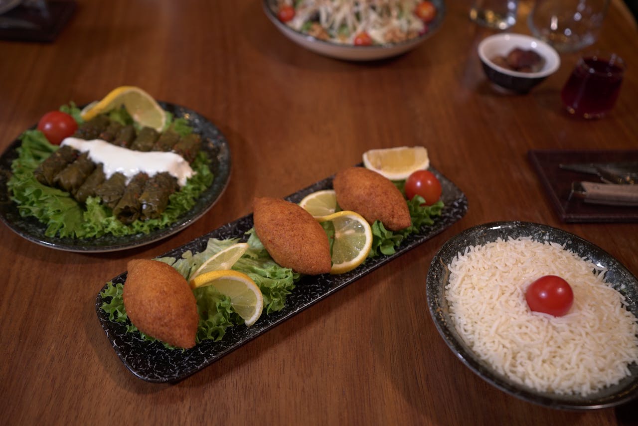Delicious Middle Eastern dishes including kibbeh, dolma, and rice served with greens and lemon slices.